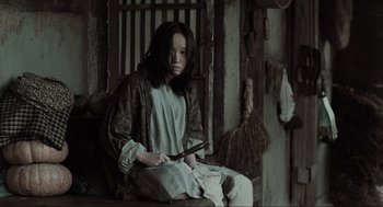Movie still from “Memories of Murder” (2003), directed by Bong Joon Ho – A woman sitting on a chair holding a knife; Medium shot, High angle