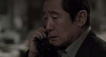 Movie still from “Memories of Murder” (2003), directed by Bong Joon Ho – An older man talking on a phone while wearing a suit; Close Up shot, High angle