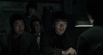 Movie still from “Memories of Murder” (2003), directed by Bong Joon Ho – A group of people sitting in a dark room; Medium shot, Over the shoulder angle