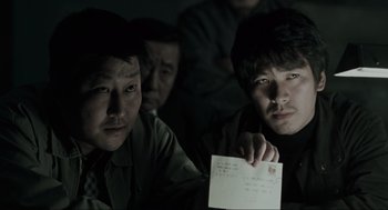 Movie still from “Memories of Murder” (2003), directed by Bong Joon Ho – A group of men sitting next to each other holding papers; Close Up shot, Over the shoulder angle