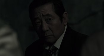Movie still from “Memories of Murder” (2003), directed by Bong Joon Ho – An older man wearing a suit and a tie; Close Up shot, Over the shoulder angle