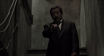 Movie still from “Memories of Murder” (2003), directed by Bong Joon Ho – An older man wearing a suit and tie smoking a cigarette; Medium shot, Low angle