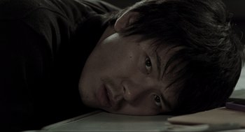 Movie still from “Memories of Murder” (2003), directed by Bong Joon Ho – A young man is laying on the floor looking at the camera; Close Up shot, High angle