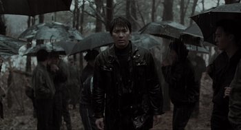 Movie still from “Memories of Murder” (2003), directed by Bong Joon Ho – A group of people standing in the rain holding umbrellas; Medium shot, Low angle