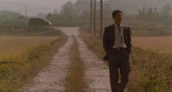 Movie still from “Memories of Murder” (2003), directed by Bong Joon Ho – A man in a suit standing on the side of a road; Wide shot, Low angle