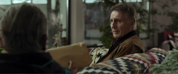 Movie still from “Memory” (2022), directed by Martin Campbell – A man sitting on a couch holding a book; Close Up shot, Over the shoulder angle