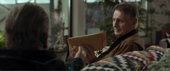 Movie still from “Memory” (2022), directed by Martin Campbell – A man sitting on a couch holding an open envelope; Close Up shot, Over the shoulder angle