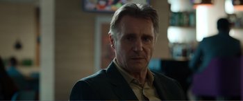 Movie still from “Memory” (2022), directed by Martin Campbell – A person wearing a suit and tie; Close Up shot, Over the shoulder angle