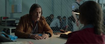 Movie still from “Memory” (2022), directed by Martin Campbell – A man sitting at a table in front of a group of people; Medium shot, Over the shoulder angle
