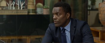 Movie still from “Memory” (2022), directed by Martin Campbell – A man wearing a suit and tie sitting at a table; Close Up shot, Over the shoulder angle