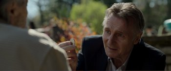 Movie still from “Memory” (2022), directed by Martin Campbell – An older man in a suit holding a piece of metal; Close Up shot, Over the shoulder angle