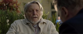 Movie still from “Memory” (2022), directed by Martin Campbell – An old man with a beard and a white beard; Close Up shot, Over the shoulder angle