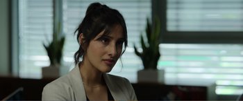 Movie still from “Memory” (2022), directed by Martin Campbell – A woman in a white jacket sitting in front of a plant; Close Up shot, Over the shoulder angle