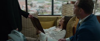Movie still from “Memory” (2022), directed by Martin Campbell – A woman sitting on a couch reading a book; Medium shot, High angle