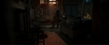 Movie still from “Memory” (2022), directed by Martin Campbell – A man standing in a room with a lot of furniture; Wide shot, High angle