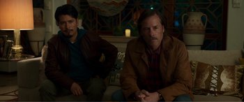 Movie still from “Memory” (2022), directed by Martin Campbell – Two people sitting on a couch in a room; Medium shot, High angle