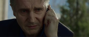 Movie still from “Memory” (2022), directed by Martin Campbell – An older man holding his hand up to his ear; Close Up shot, Low angle