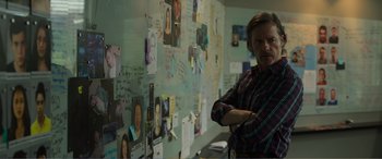 Movie still from “Memory” (2022), directed by Martin Campbell – A man standing in front of a wall covered in pictures; Medium shot, Over the shoulder angle