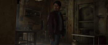 Movie still from “Memory” (2022), directed by Martin Campbell – A man in a brown jacket standing next to a table; Medium shot, Low angle