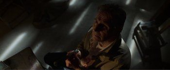 Movie still from “Memory” (2022), directed by Martin Campbell – An older man holding a cell phone in a dark room; Close Up shot, High angle