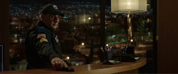 Movie still from “Memory” (2022), directed by Martin Campbell – A man sitting at a counter in front of a window at night; Medium shot, Low angle