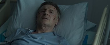Movie still from “Memory” (2022), directed by Martin Campbell – A man laying in a hospital bed in a hospital room; Close Up shot, Low angle