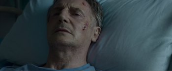 Movie still from “Memory” (2022), directed by Martin Campbell – A person laying in a bed with a bandage on his face; Close Up shot, Low angle