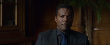 Movie still from “Memory” (2022), directed by Martin Campbell – A man wearing a suit and tie in front of a wall; Close Up shot, Low angle