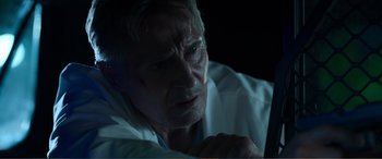Movie still from “Memory” (2022), directed by Martin Campbell – An older man in a white lab coat looks at the camera; Close Up shot, Low angle
