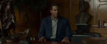 Movie still from “Memory” (2022), directed by Martin Campbell – A man sitting at a table in front of a plant; Medium shot, Over the shoulder angle