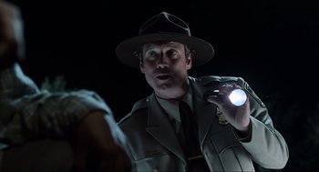 Movie still from “Men in Black” (1997), directed by Barry Sonnenfeld – A man in a hat holding a flashlight in a dark room; Close Up shot, Over the shoulder angle
