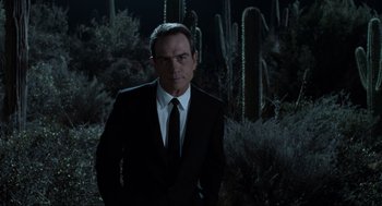 Movie still from “Men in Black” (1997), directed by Barry Sonnenfeld – A man in a suit and tie standing in a field; Medium shot, Over the shoulder angle