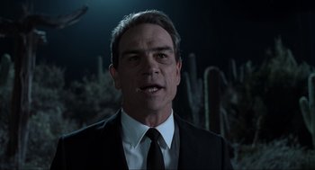 Movie still from “Men in Black” (1997), directed by Barry Sonnenfeld – A man in a black suit and white tie; Close Up shot, Over the shoulder angle
