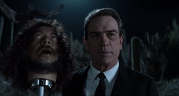 Movie still from “Men in Black” (1997), directed by Barry Sonnenfeld – A man in a suit and tie standing next to another man in a suit and tie; Close Up shot, Over the shoulder angle