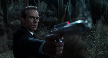 Movie still from “Men in Black” (1997), directed by Barry Sonnenfeld – A man holding a gun in his hand; Close Up shot, Low angle