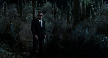 Movie still from “Men in Black” (1997), directed by Barry Sonnenfeld – A man in a suit and tie standing in the woods; Wide shot, High angle