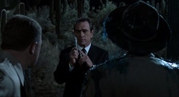 Movie still from “Men in Black” (1997), directed by Barry Sonnenfeld – A man in a suit and tie holding a cell phone; Close Up shot, Over the shoulder angle