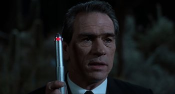 Movie still from “Men in Black” (1997), directed by Barry Sonnenfeld – A man in a suit holding a pen in his hand; Close Up shot, Over the shoulder angle