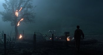 Movie still from “Men in Black” (1997), directed by Barry Sonnenfeld – A man standing in a field near a fire pit at night; Extreme Wide shot, Low angle