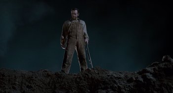 Movie still from “Men in Black” (1997), directed by Barry Sonnenfeld – A man standing on top of a dirt hill holding a rifle; Medium shot, Low angle