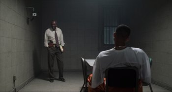 Movie still from “Men in Black” (1997), directed by Barry Sonnenfeld – A man standing next to another man sitting in a room; Wide shot, Over the shoulder angle