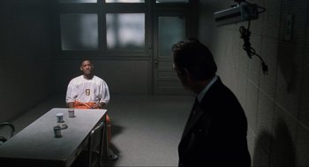 Movie still from “Men in Black” (1997), directed by Barry Sonnenfeld – A man in a suit and tie in a room with another man; Medium shot, Over the shoulder angle