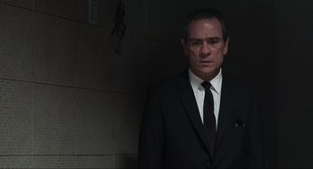 Movie still from “Men in Black” (1997), directed by Barry Sonnenfeld – A man in a suit and tie standing in front of a brick wall; Medium shot, Low angle