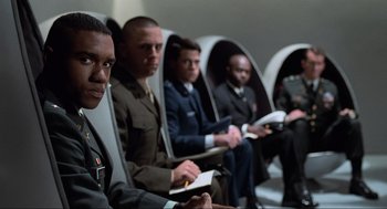 Movie still from “Men in Black” (1997), directed by Barry Sonnenfeld – A group of men sitting in a row of chairs; Medium shot, Low angle