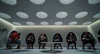 Movie still from “Men in Black” (1997), directed by Barry Sonnenfeld – A group of men sitting in a pod chair; Wide shot, Low angle