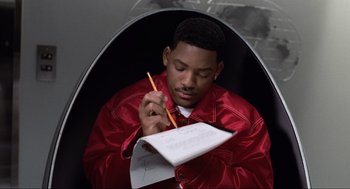 Movie still from “Men in Black” (1997), directed by Barry Sonnenfeld – A man in red jacket writing on a piece of white paper; Medium shot, High angle