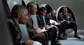 Movie still from “Men in Black” (1997), directed by Barry Sonnenfeld – A group of men sitting next to each other; Wide shot, High angle