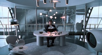 Movie still from “Men in Black” (1997), directed by Barry Sonnenfeld – A man sitting at a table in front of a large window; Wide shot, High angle
