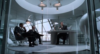 Movie still from “Men in Black” (1997), directed by Barry Sonnenfeld – A group of men sitting at a table in front of a window; Wide shot, Low angle
