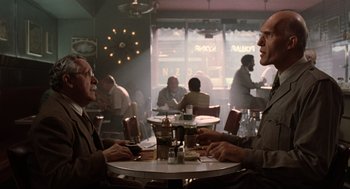 Movie still from “Men in Black” (1997), directed by Barry Sonnenfeld – Two men sitting at a table in front of a window; Medium shot, Low angle